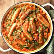 Sausage and bean casserole with vegetables and herbs in large white pan.