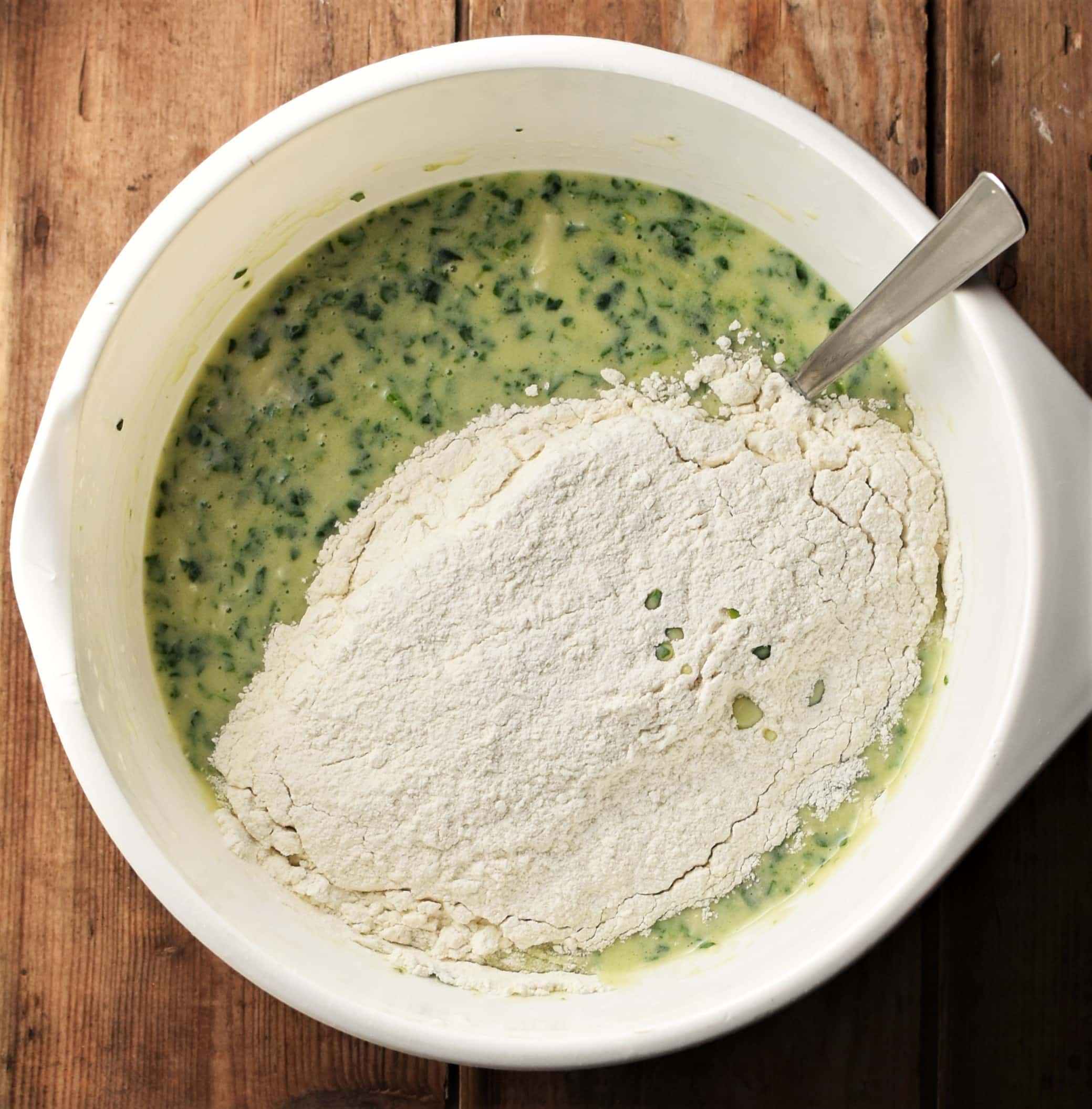 Spinach egg mixture with flour in large white bowl with spoon.