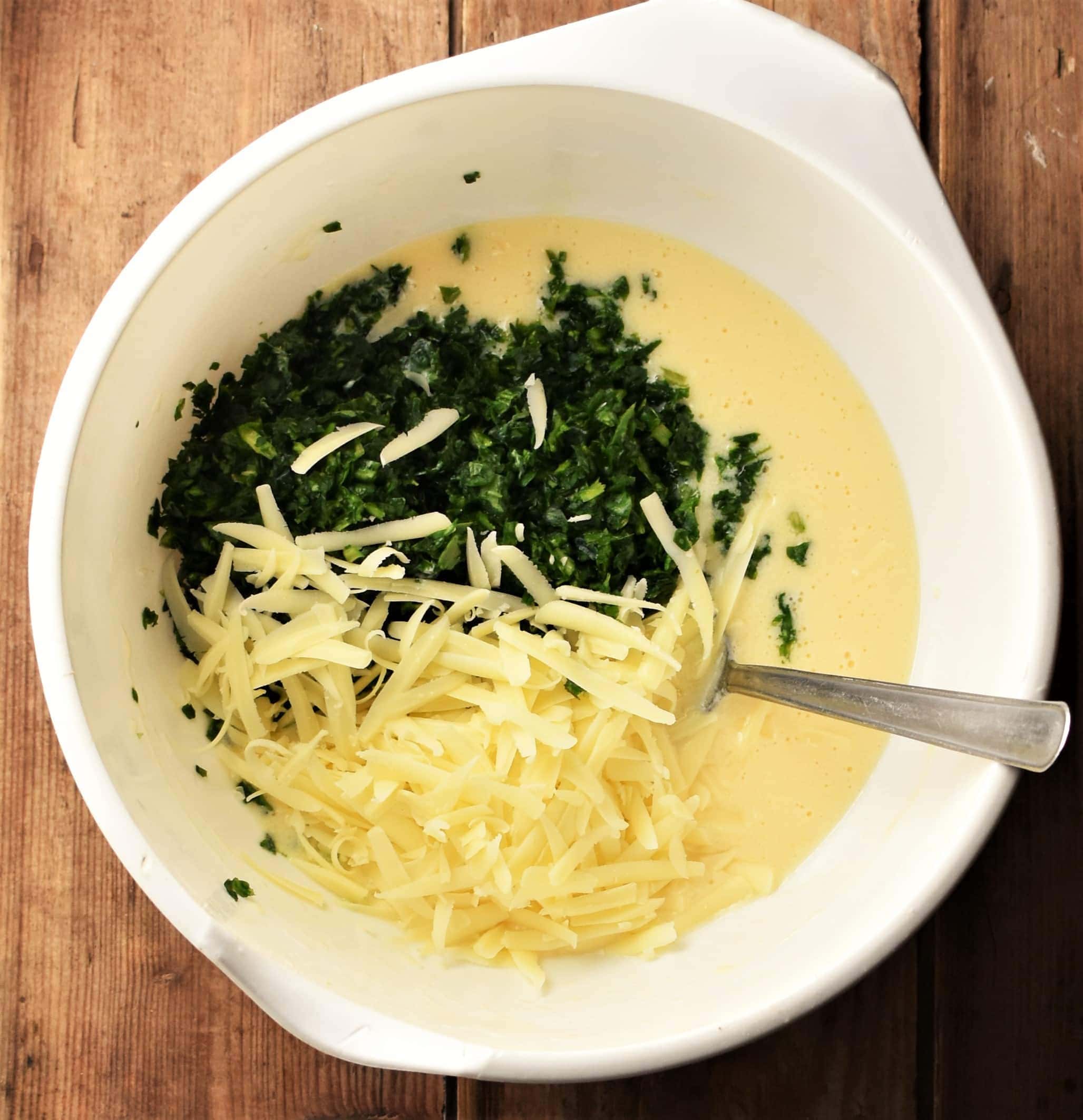 Grated cheese, chopped spinach and egg mixture in large white bowl with spoon.