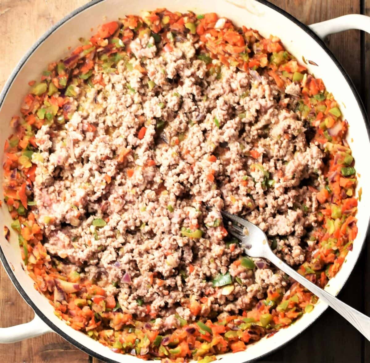 Top down view of ground meat and vegetable sauce in large white pan with fork.