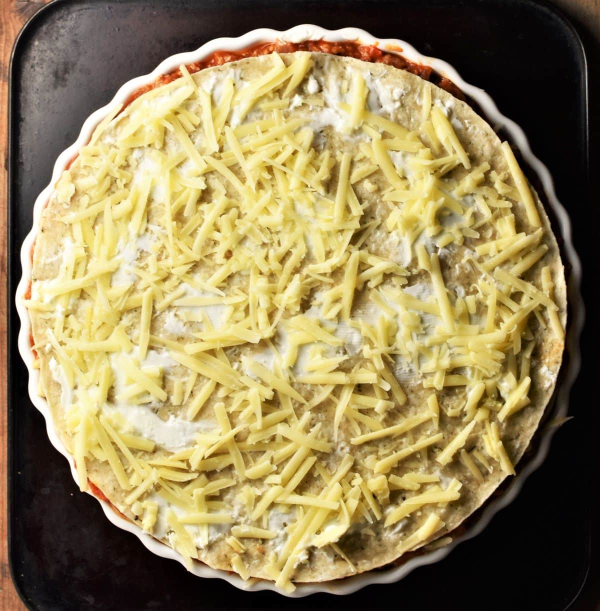 Unbaked tortilla casserole with grated cheese scattered on top.