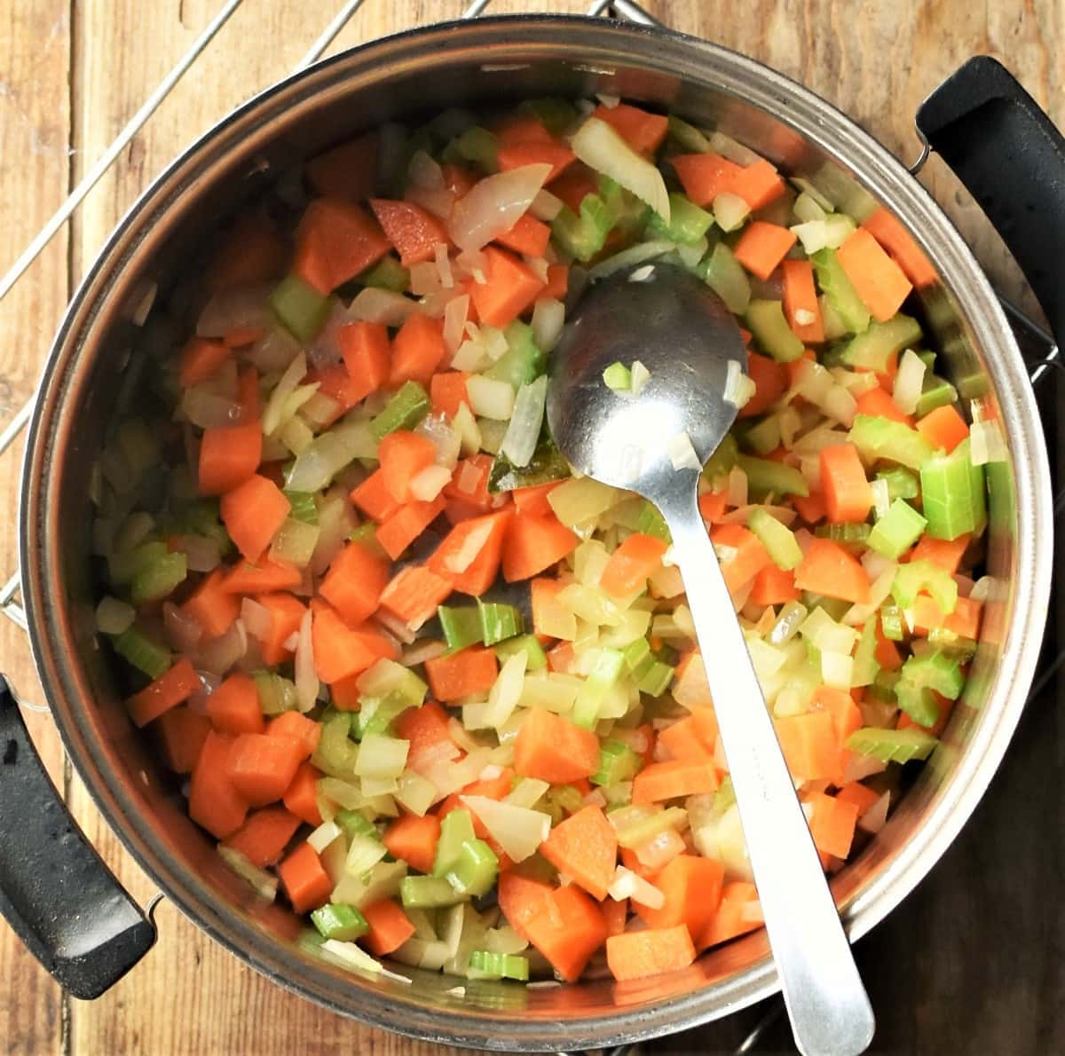 Chopped carrot, onion and celery in pot with spoon.