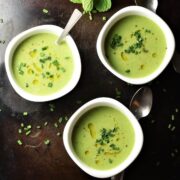Top down view of creamy cucumber pea soup in 3 white bowls with spoons.