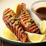 Close-up view of grilled marinated salmon with lemon wedges and hoisin sauce.