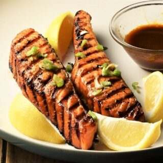 Close-up view of grilled marinated salmon with lemon wedges and hoisin sauce.