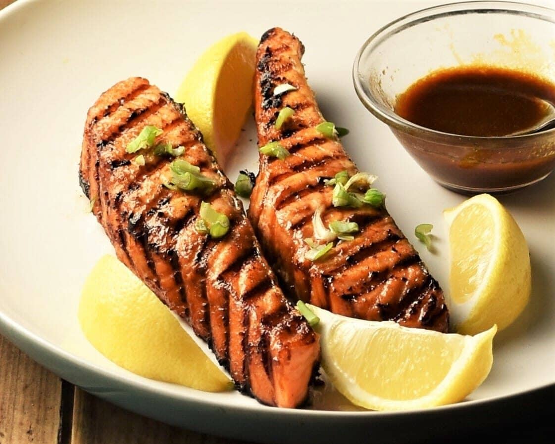 Close-up view of grilled marinated salmon with lemon wedges and hoisin sauce.