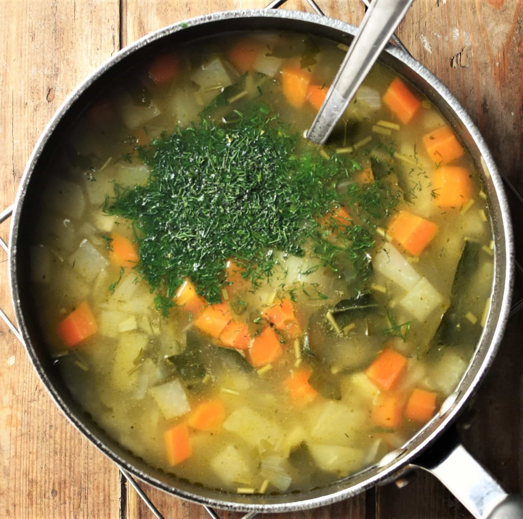 Chunky vegetable soup with fresh dill in pot with spoon.