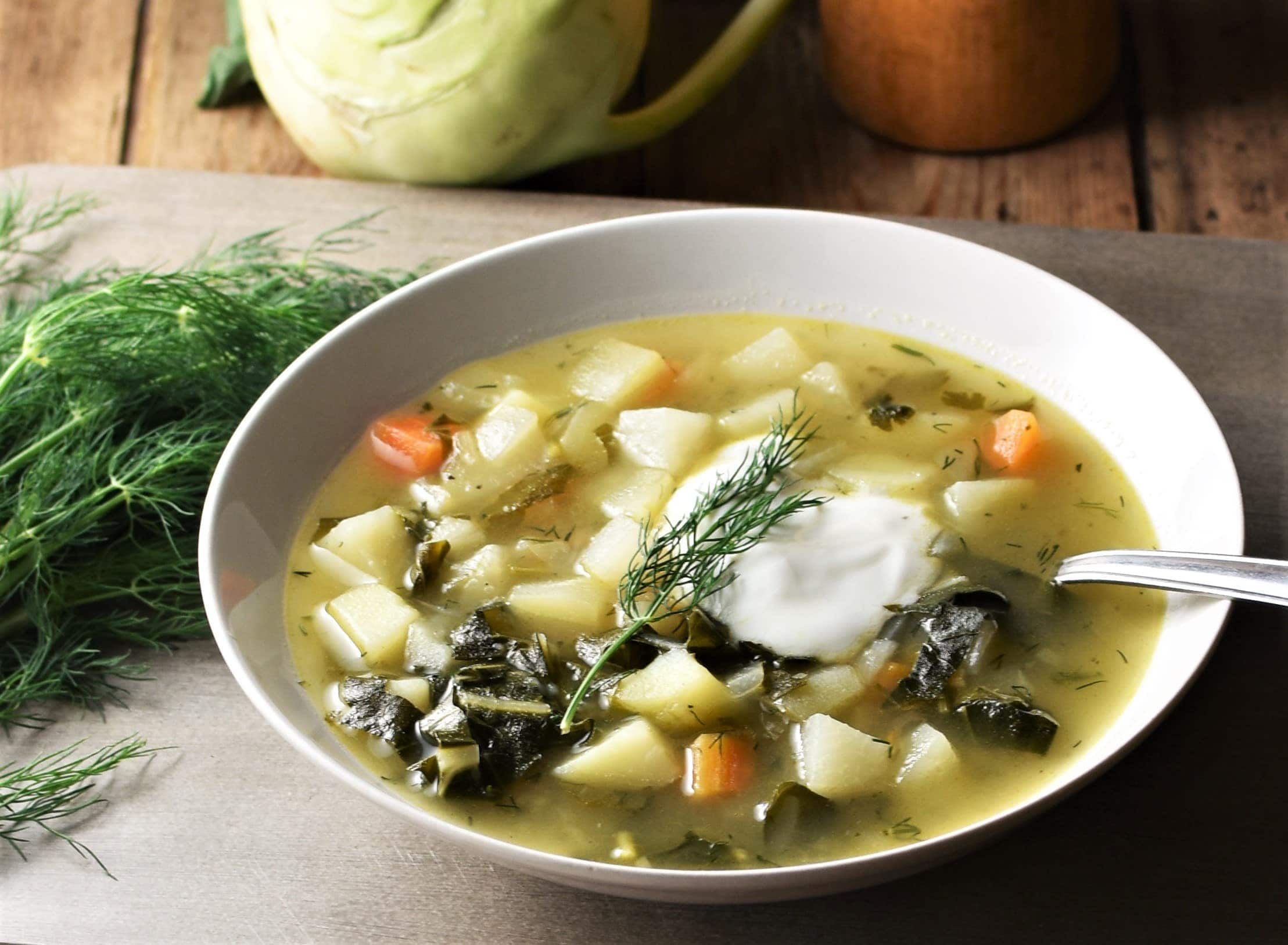 Side view of chunky vegetable soup with yogurt in white bowl with spoon.