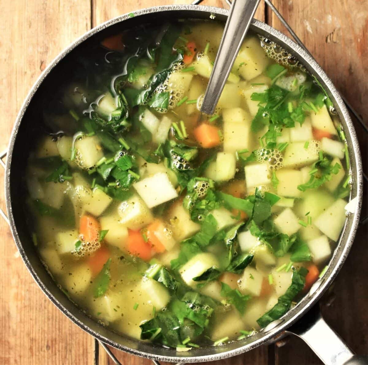 Chunky kohlrabi and vegetable soup in pot with spoon.