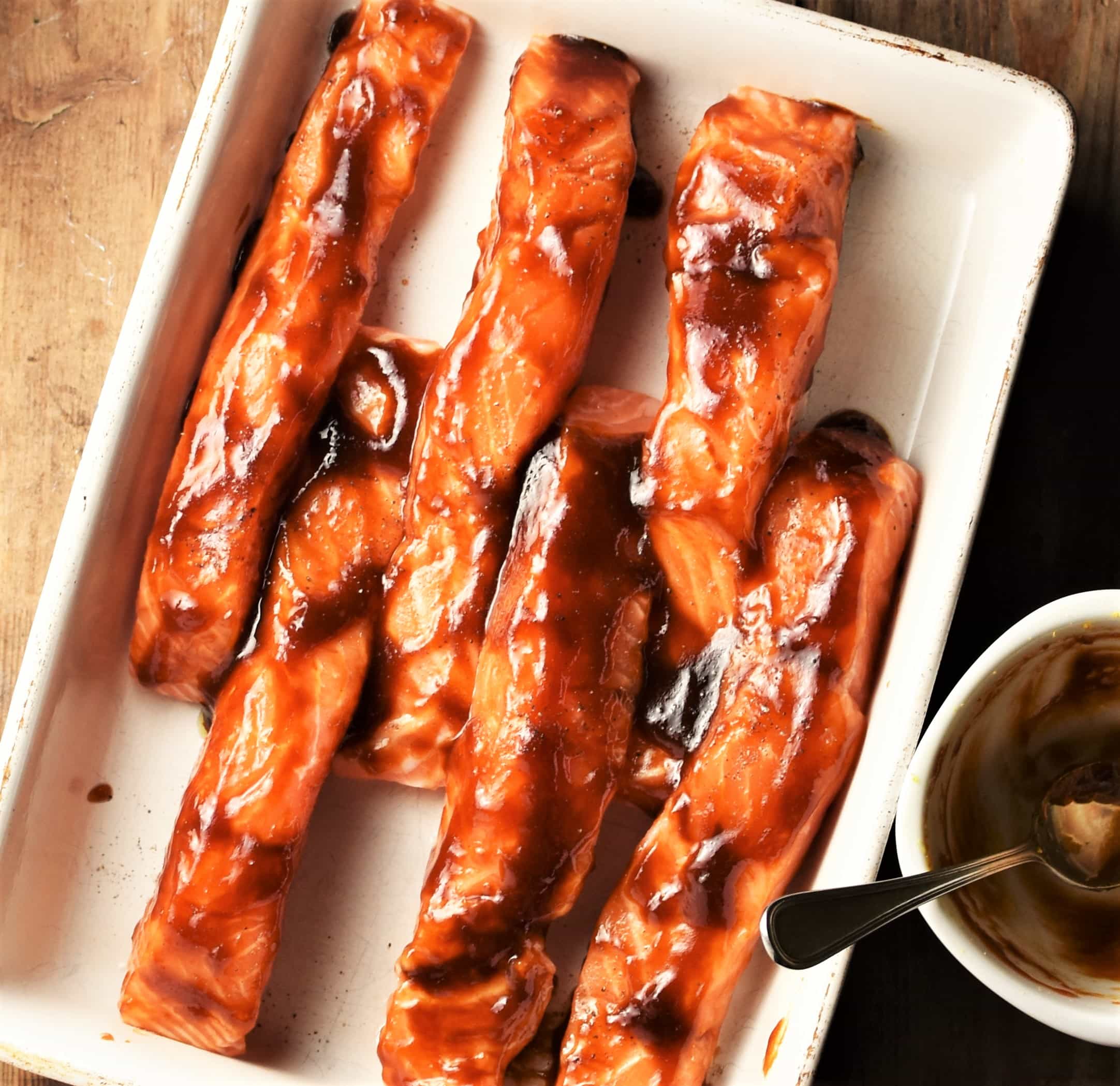 Top down view of salmon strips in hoisin marinade in white shallow dish.