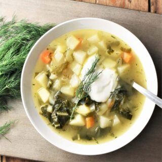 Chunky kohlrabi soup with vegetables and dollop of yogurt in white bowl with spoon and dill to the left.