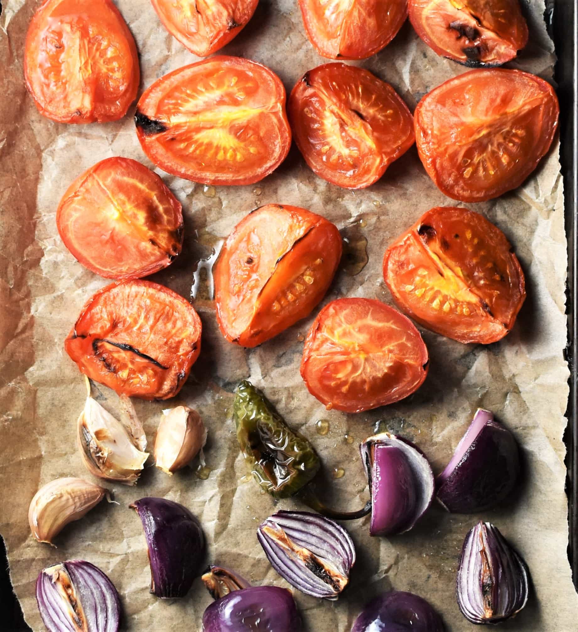 Roasted chopped tomatoes, red onions, unpeeled garlic and jalapeno on top of parchment.