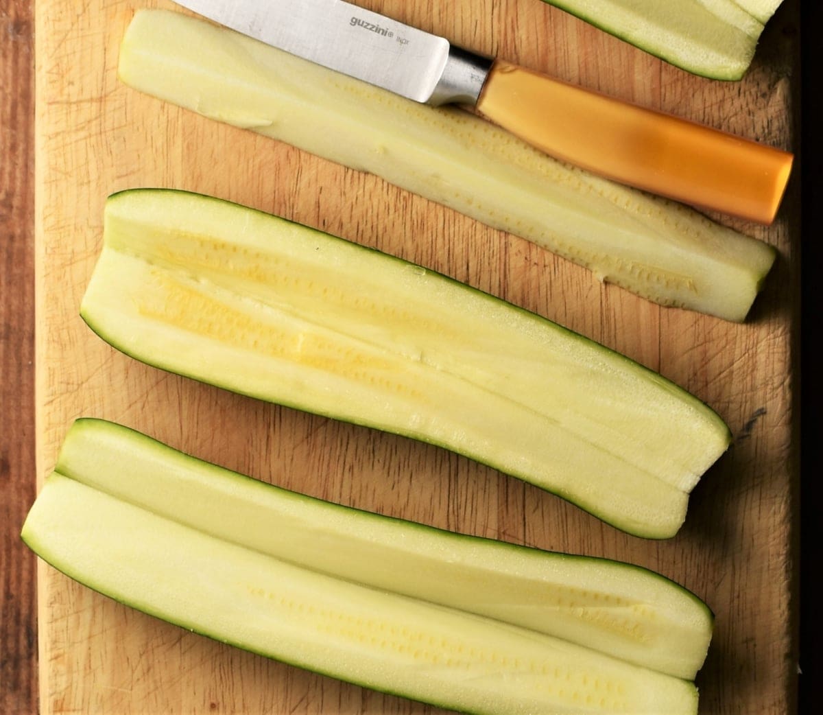 Preparing zucchini for stuffing by removing middle with knife.
