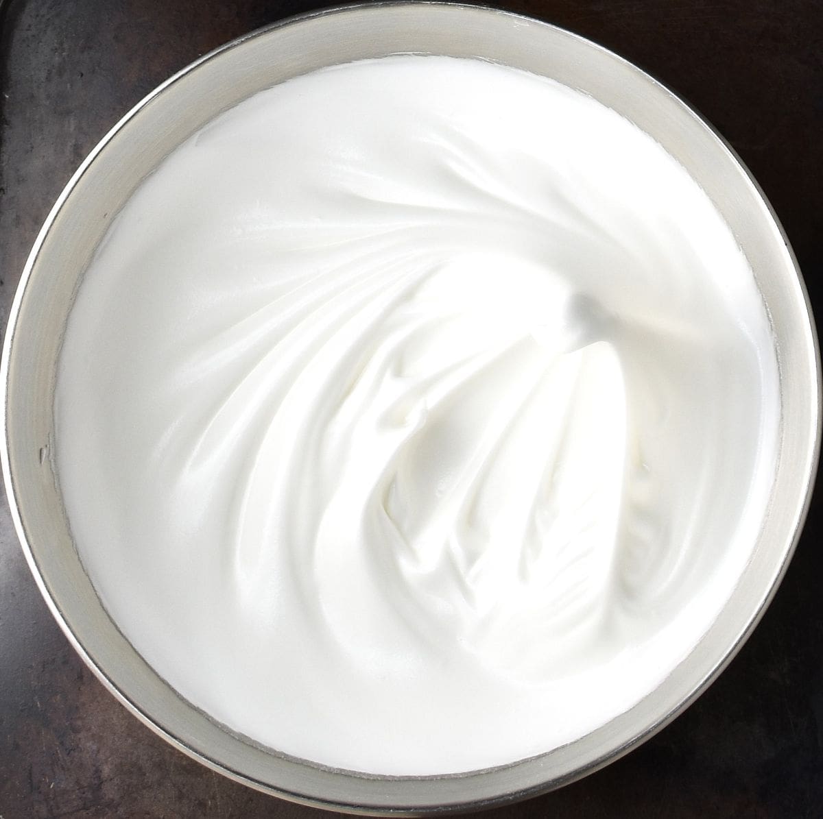 Top down view of soft meringue mixture in metal bowl.