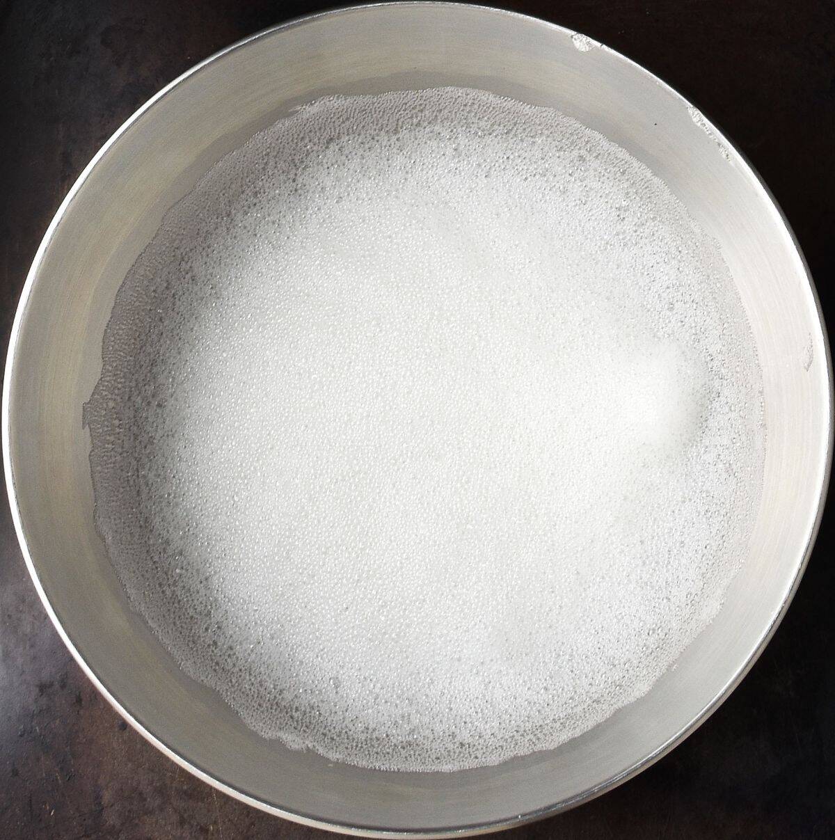 Foamy egg white mixture in metal bowl.