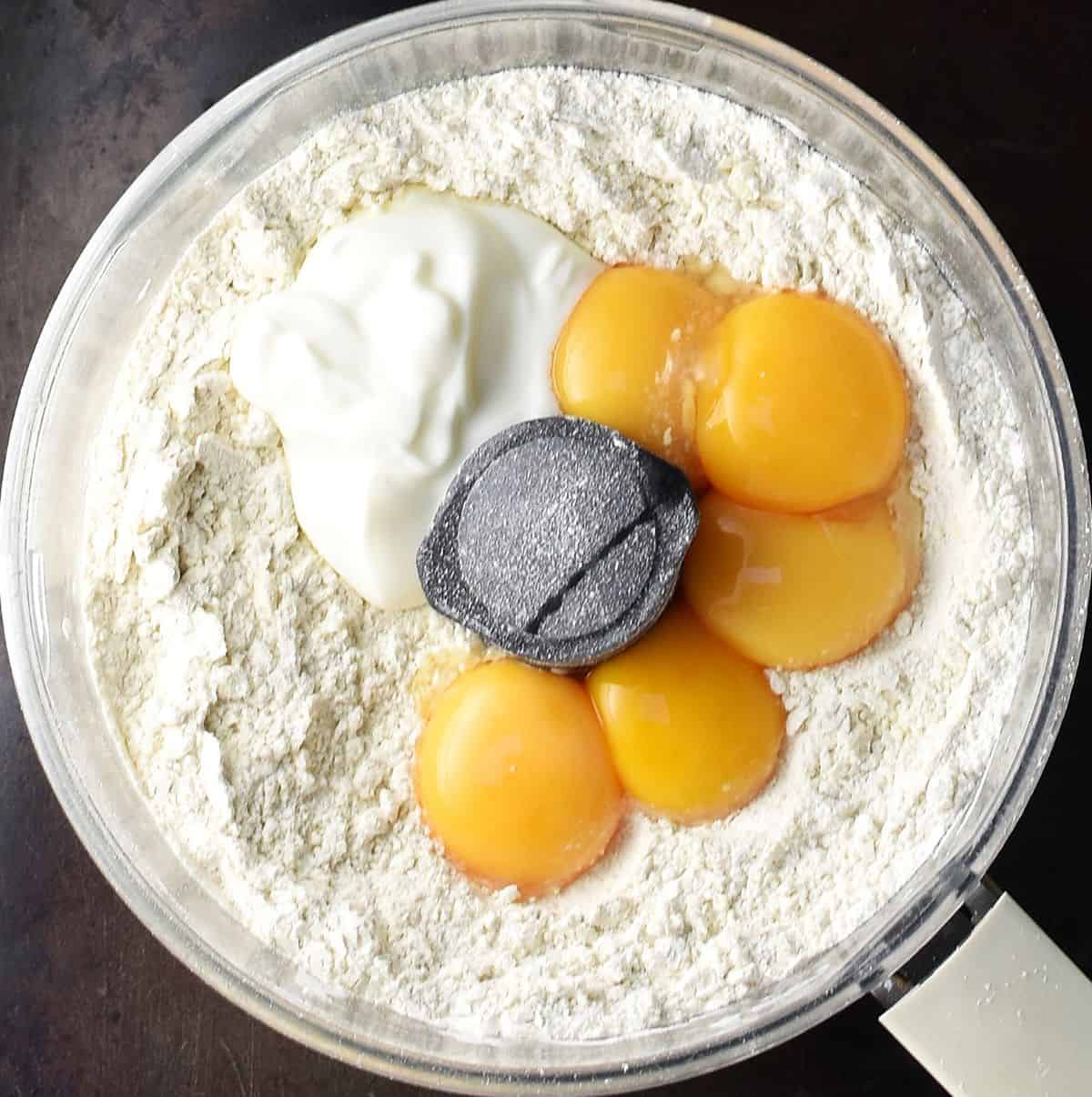 5 egg yolks and yogurt on top of floury mixture in food processor bowl.