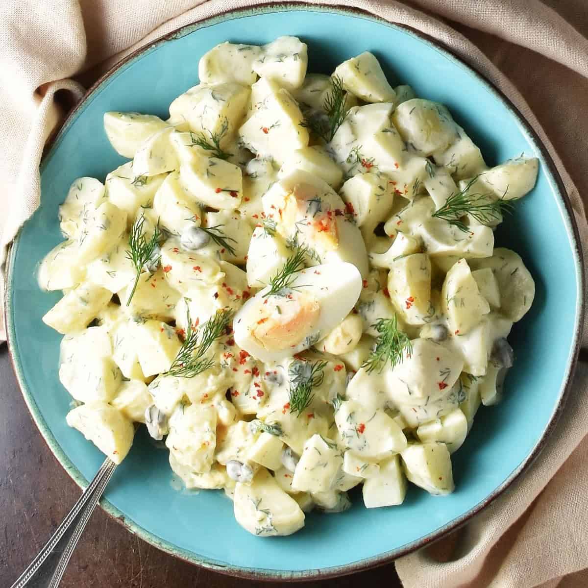 Top down view of potato dill salad with eggs in blue bowl with spoon.