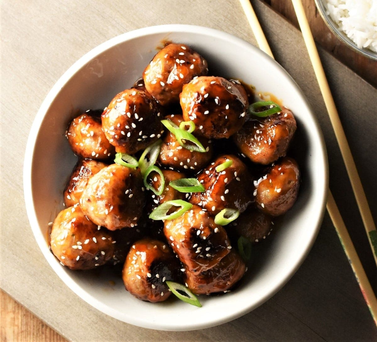 Top down view of meatballs in white bowl with chopsticks in background.