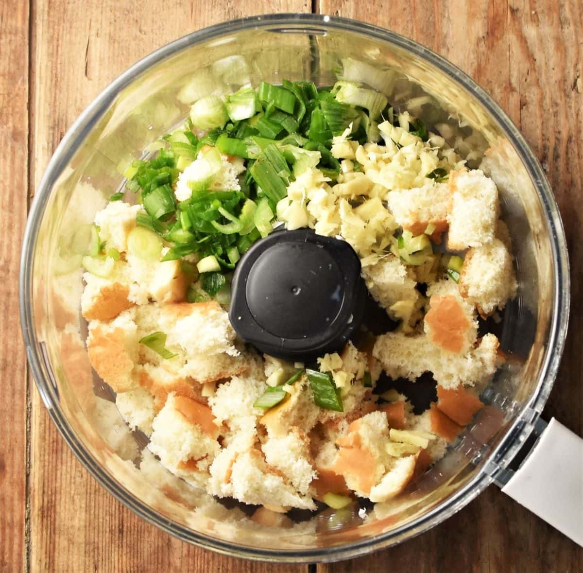 Torn bread and chopped green onion in food processor bowl.