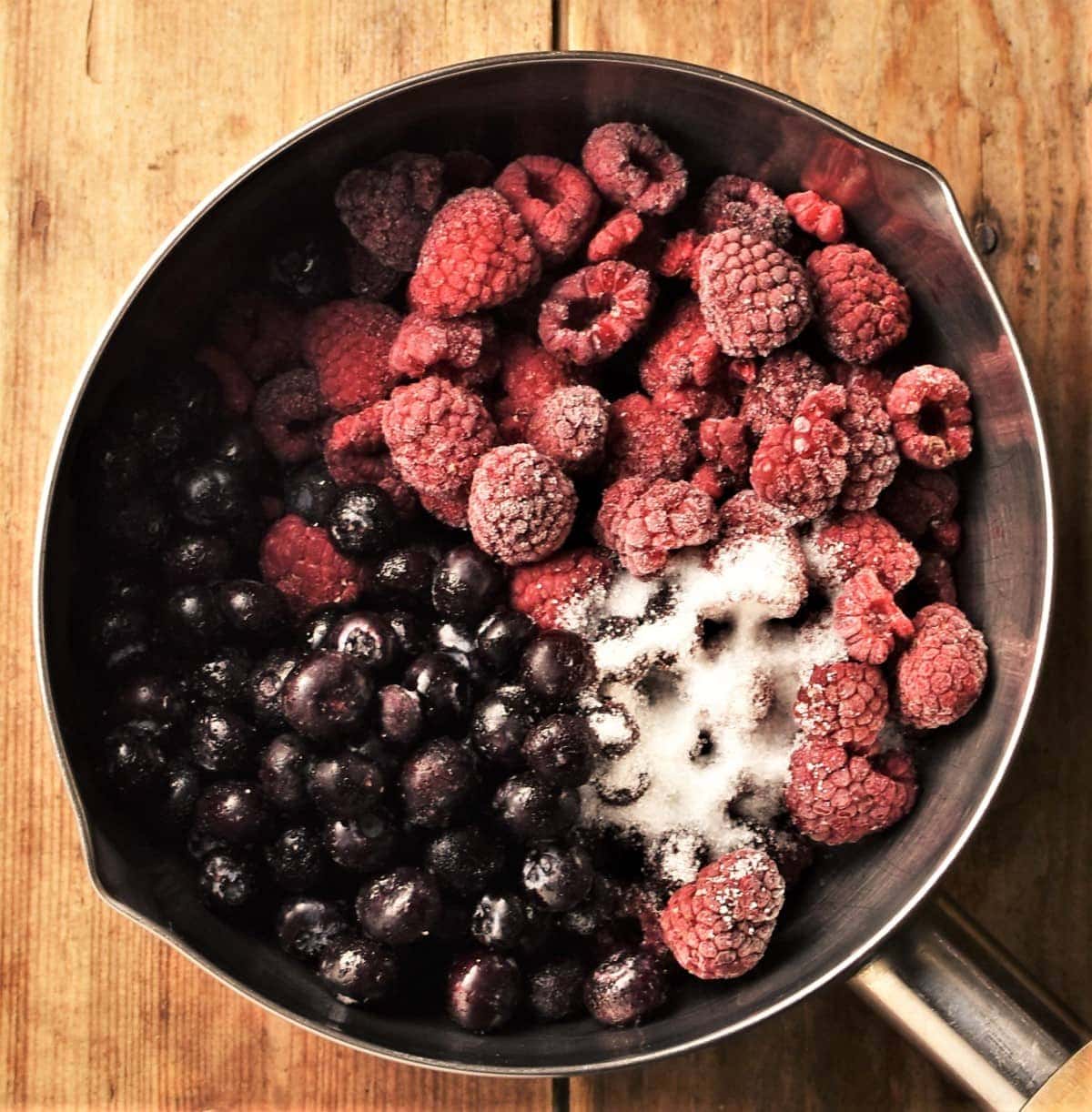 Frozen fruit and sugar in saucepan.