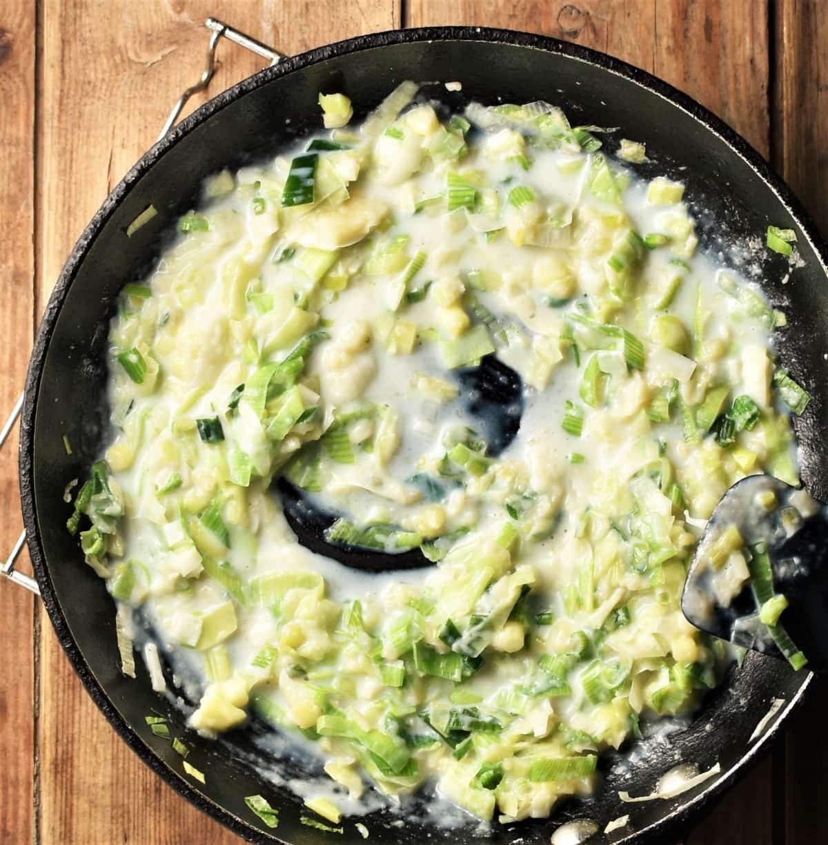Chopped leek in creamy white sauce in pan.