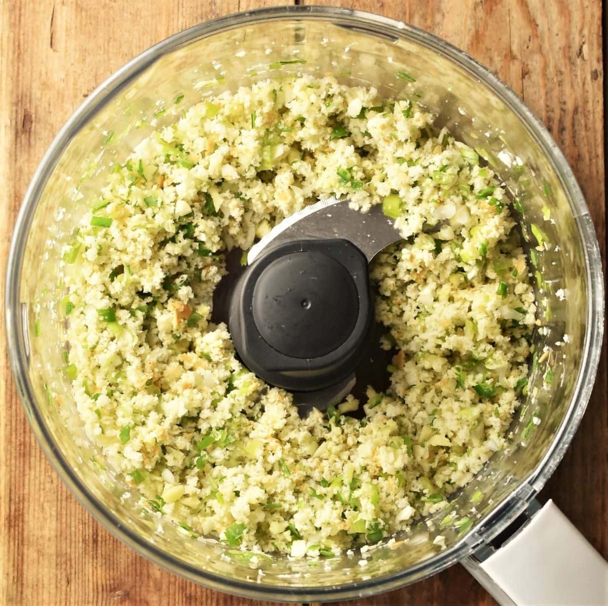 Crumbly bread and herb mixture in food processor bowl.