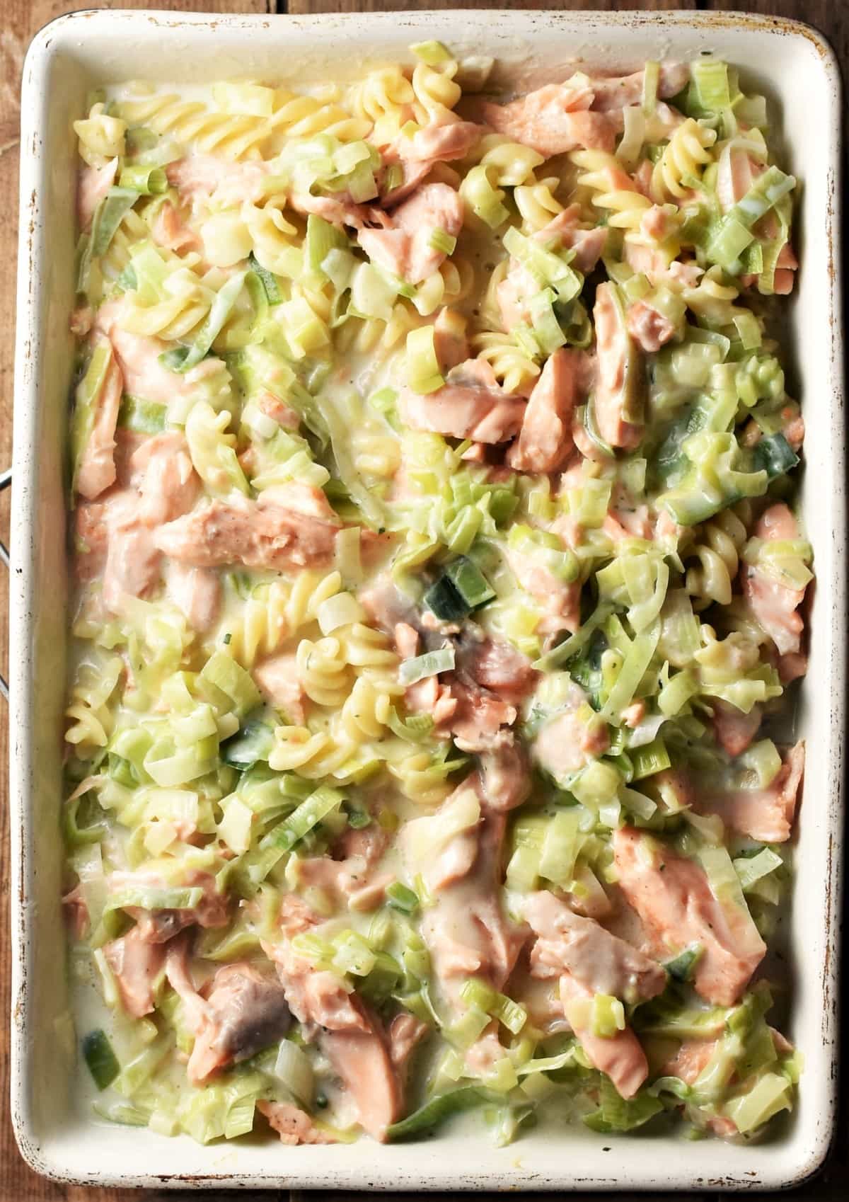 Fusilli pasta with salmon chunks and creamy leek sauce in casserole dish.