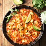 Shrimp in tomato coconut sauce with lime wedges and herbs in pan.