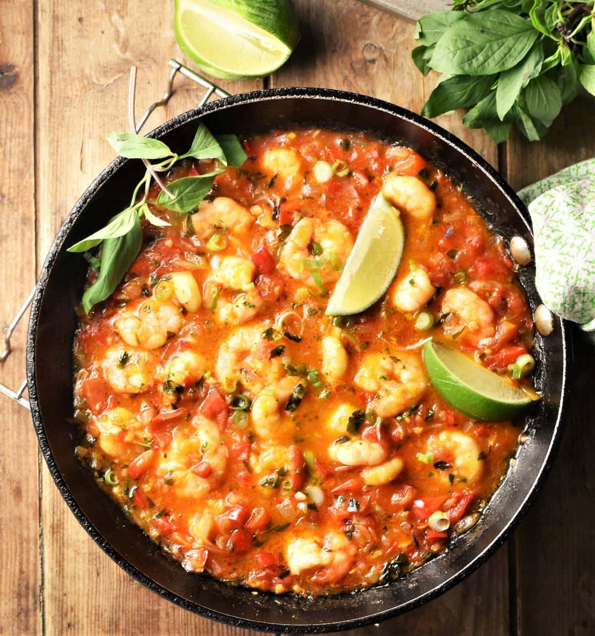 Shrimp in tomato coconut sauce with lime wedges and herbs in pan.