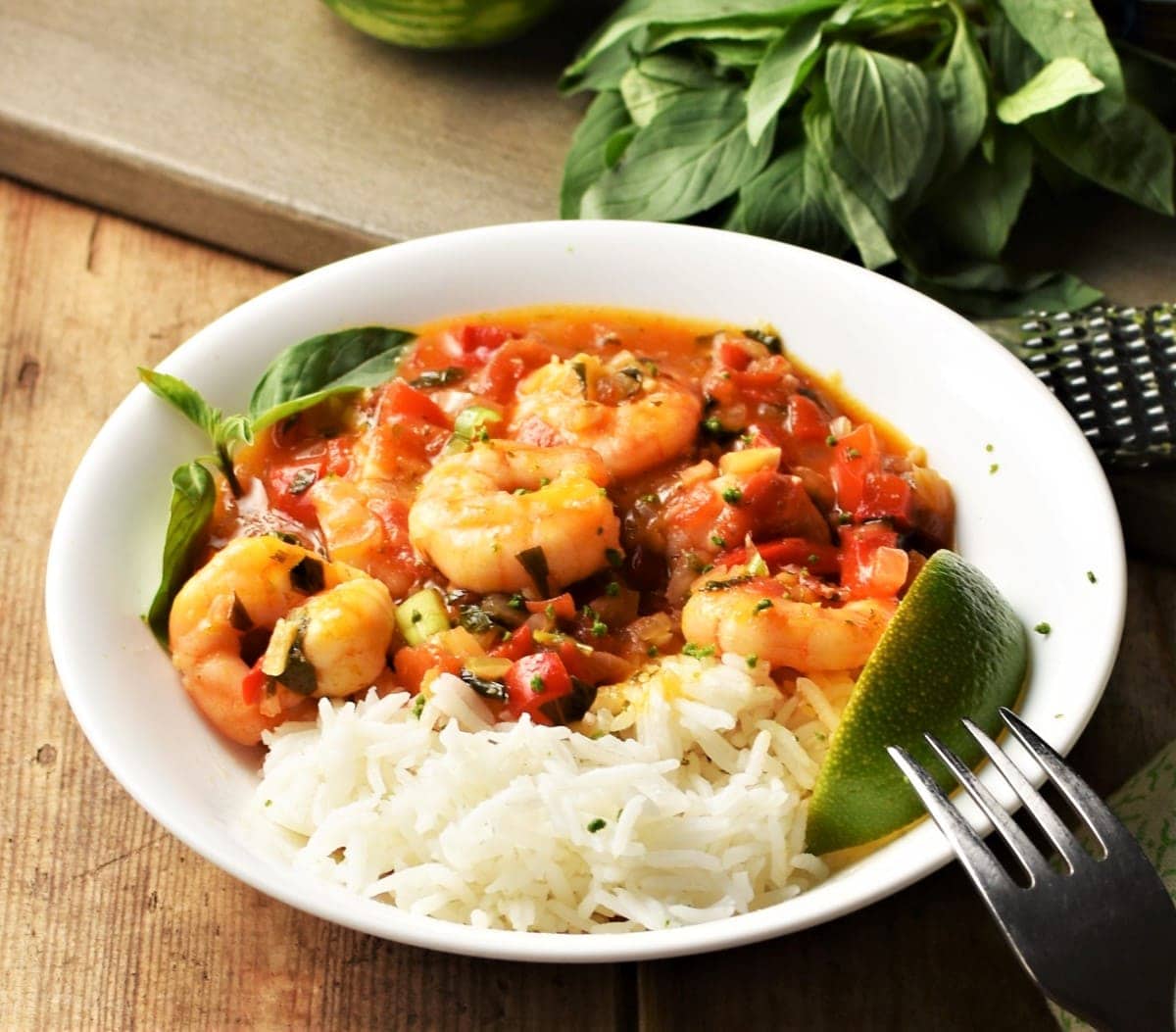 Side view of rice with shrimp in tomato sauce with lime wedges in white bowl.