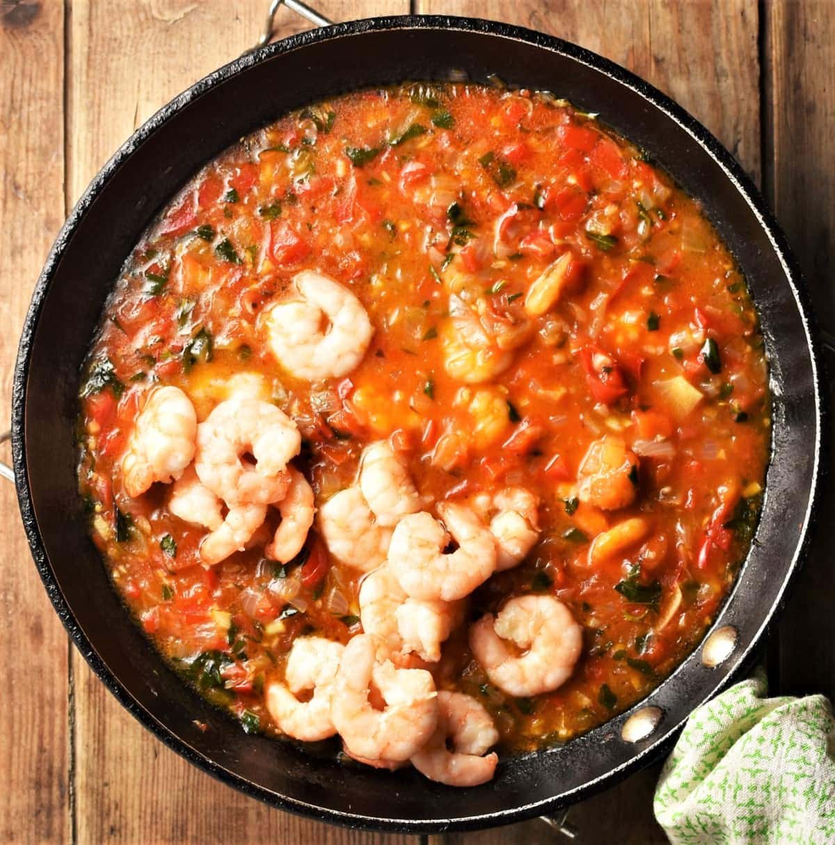 Cooked shrimp being added into tomato sauce in pan.