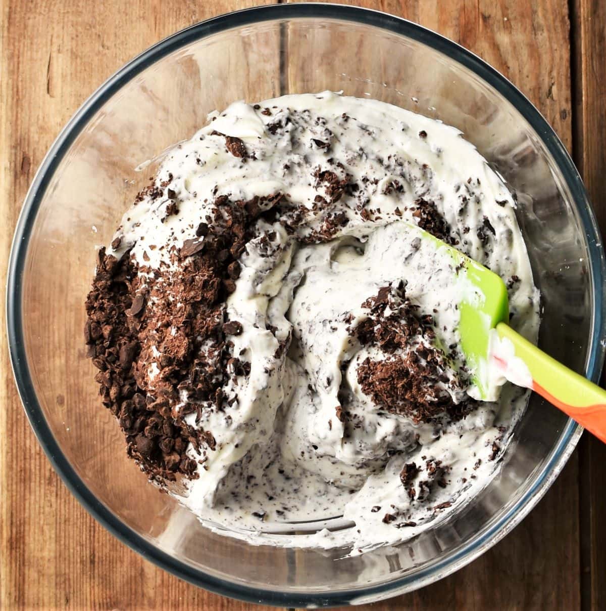 Cheesecake mixture with chocolate shavings in bowl with green spatula.