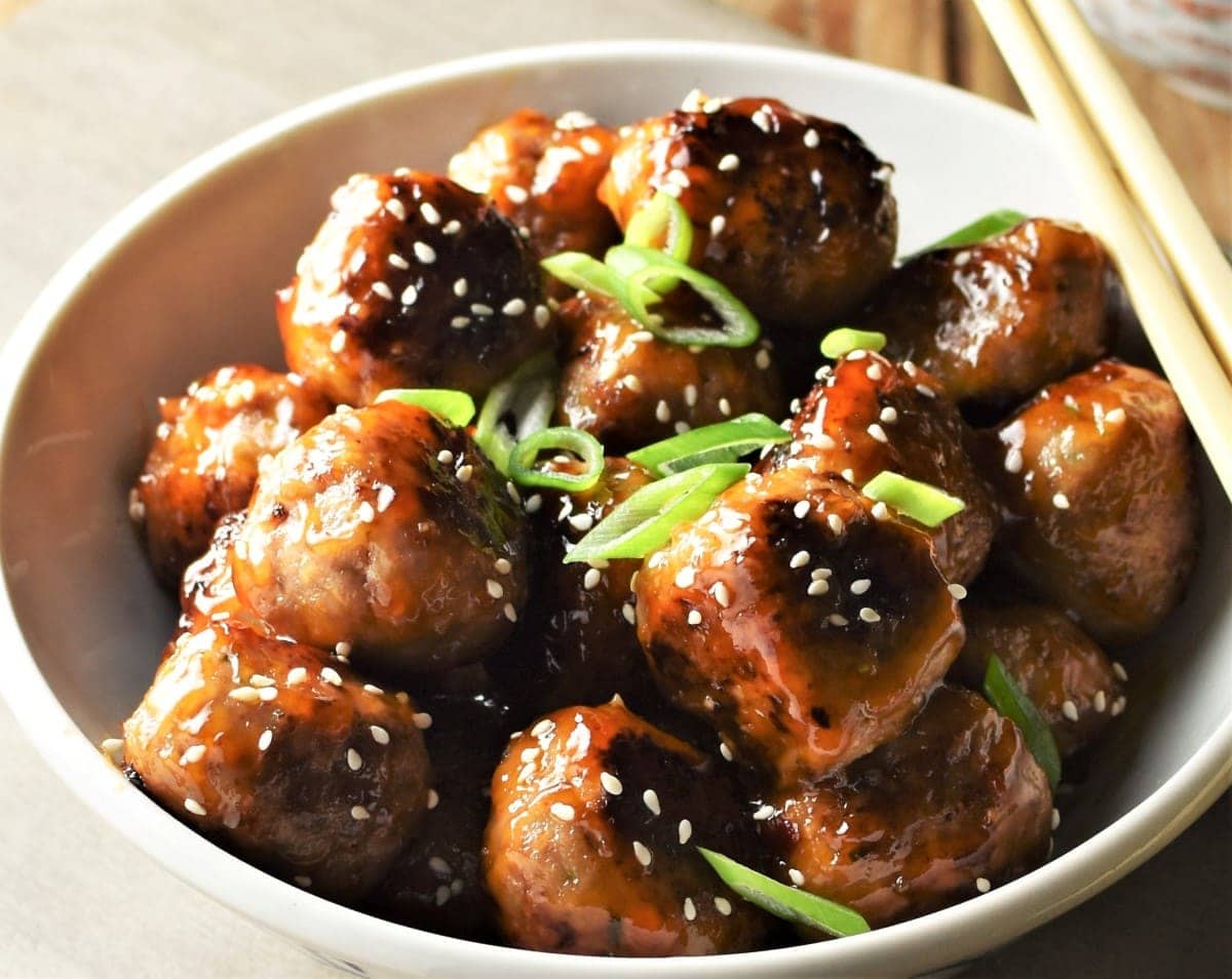 Close-up view of meatballs with chilli glaze, sesame seeds and green onion.