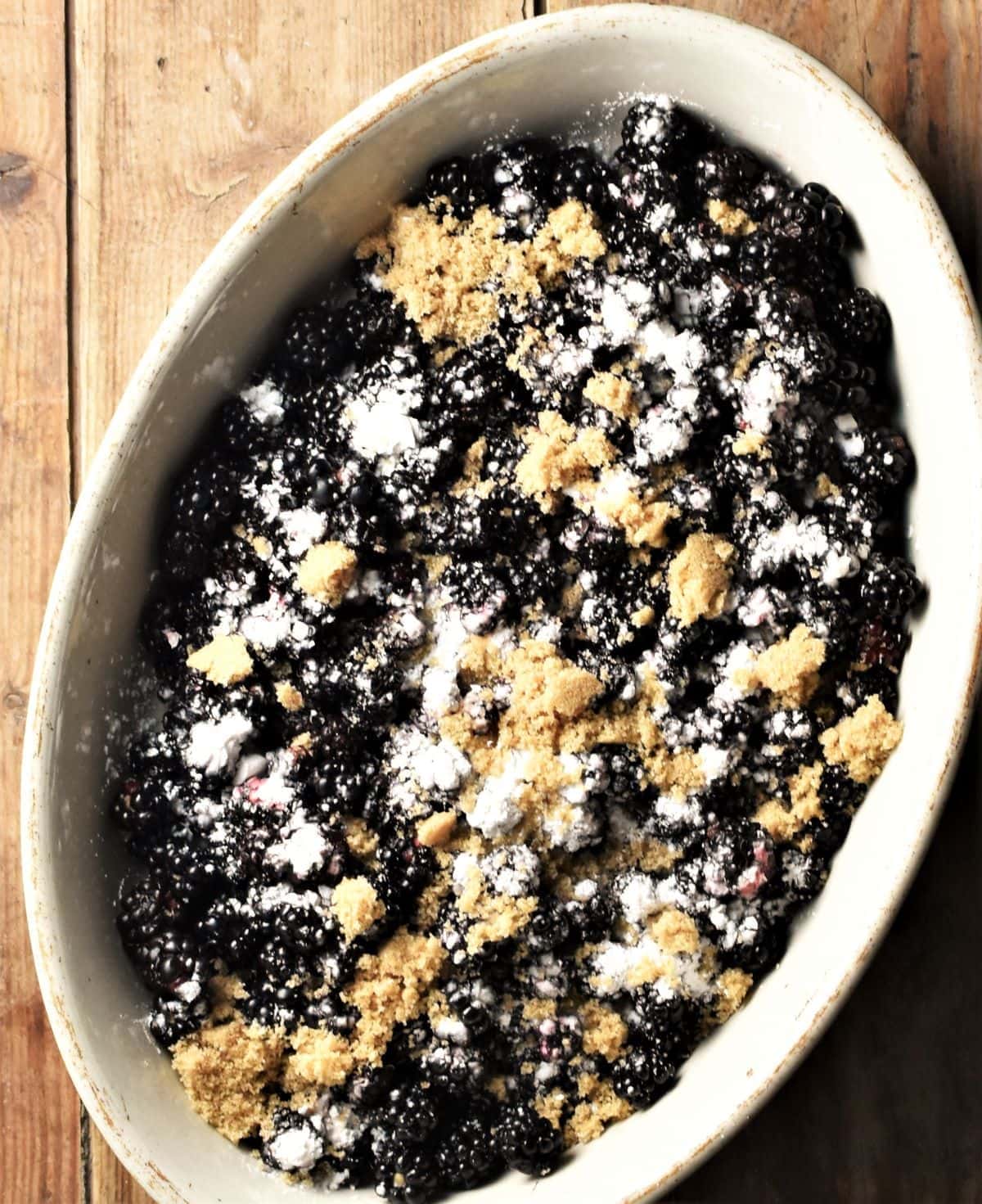 Blackberries with flour and brown sugar in white oval dish.