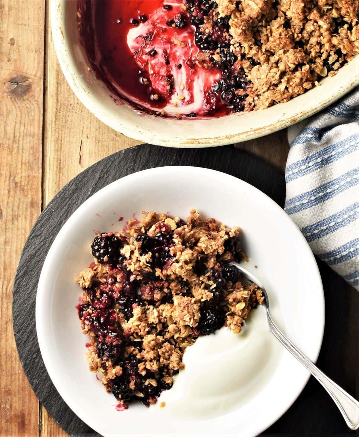Blackberry crumble with yogurt and spoon in white bowl.