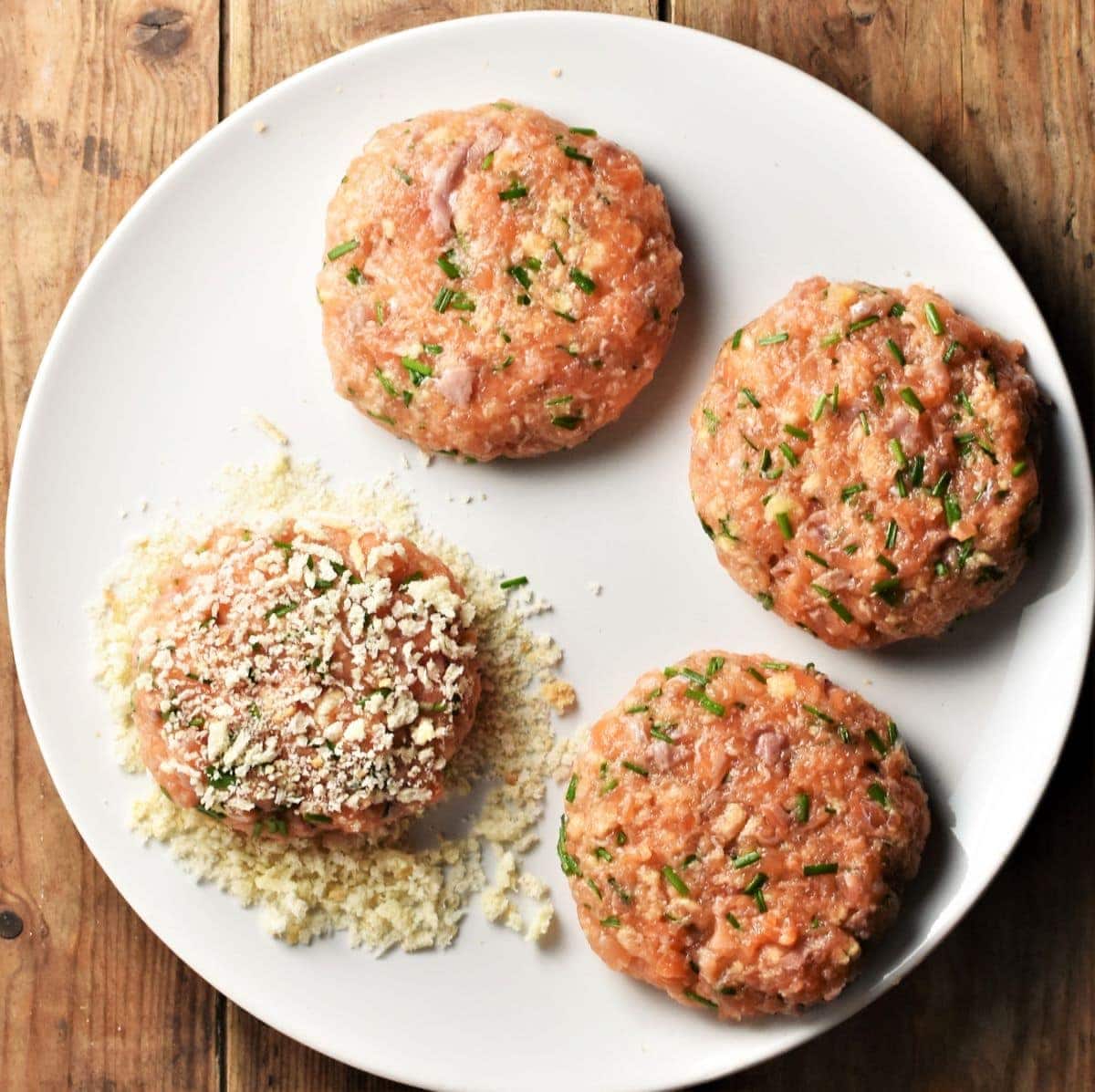 4 salmon burgers with breadcrumbs on large plate.