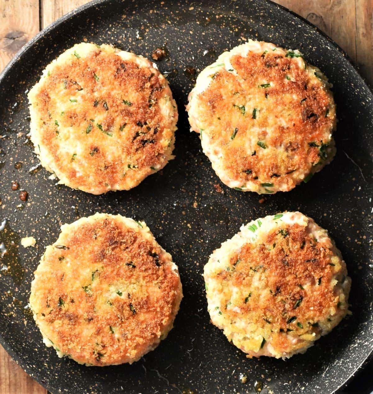 4 crispy salmon burgers on top of pan.