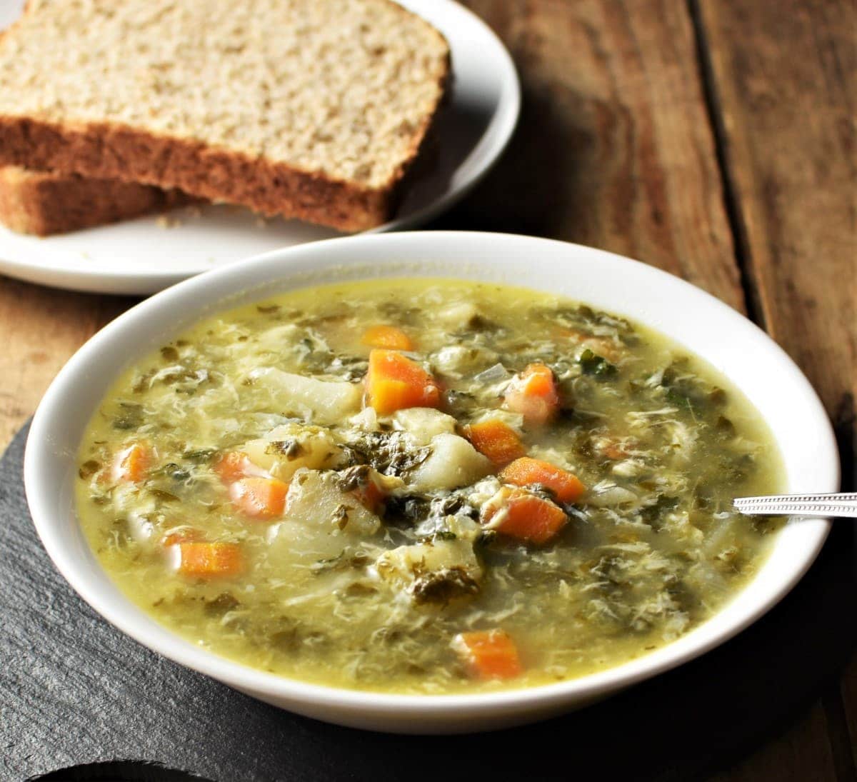 Side view of sorrel soup in bowl with spoon and bread in background.