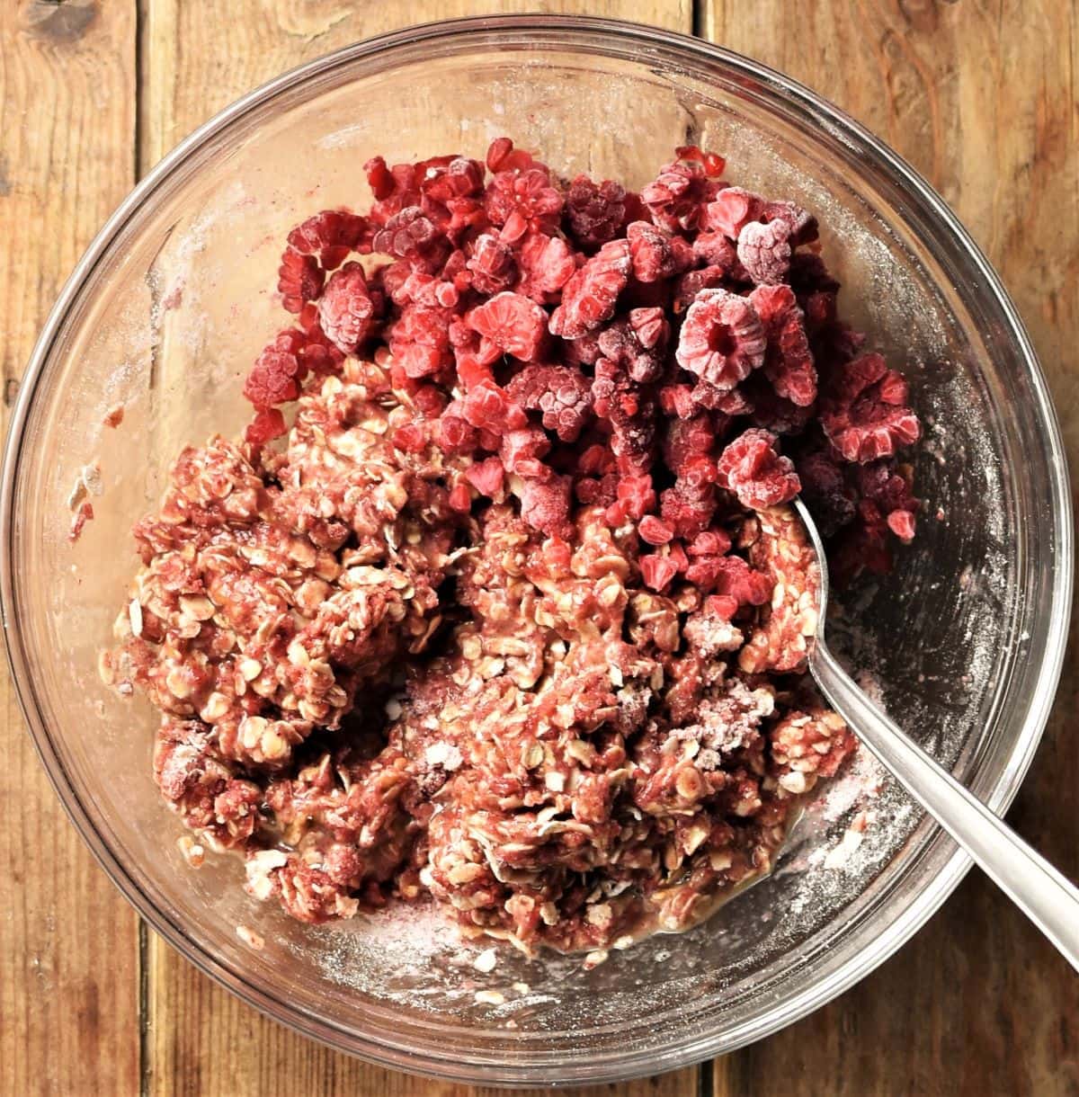 Raspberry cookies batter with chunks of raspberries and spoon in bowl.