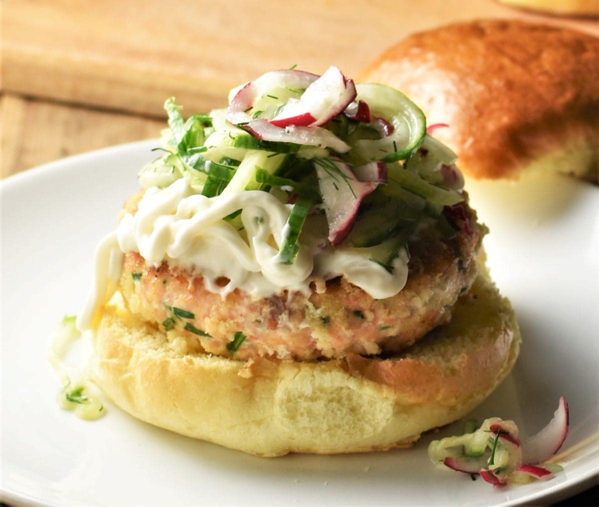 Side view of salmon burger topped with slaw and mayonnaise.