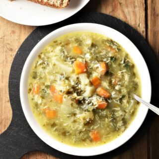 Top down view of sorrel soup with vegetables in white bowl with spoon.