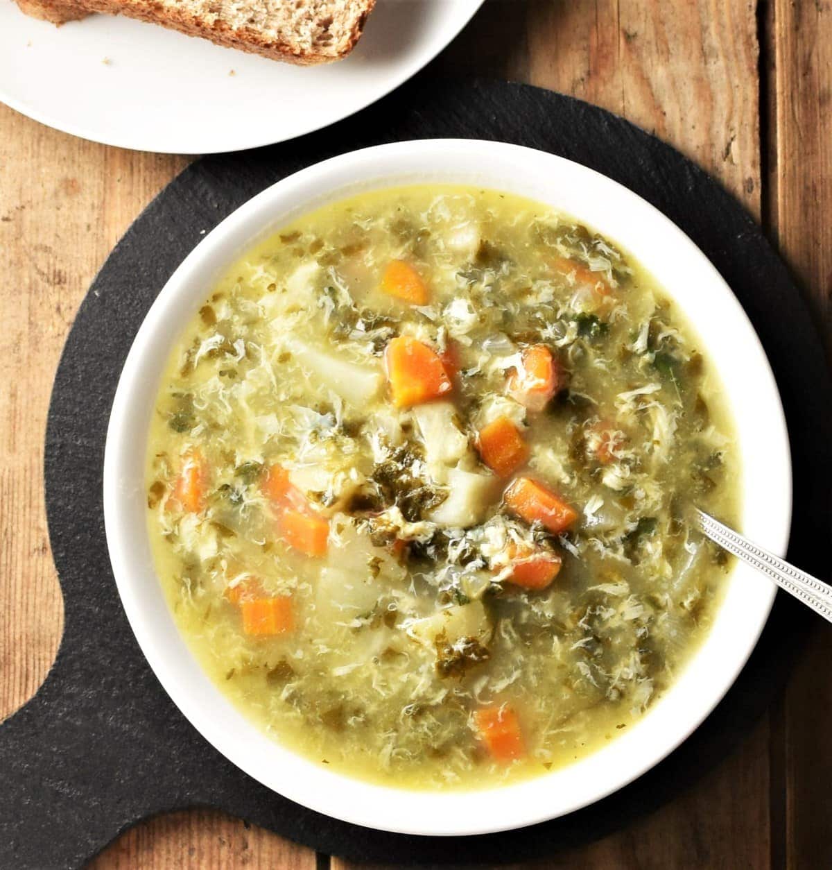 Top down view of sorrel soup with vegetables in white bowl with spoon.