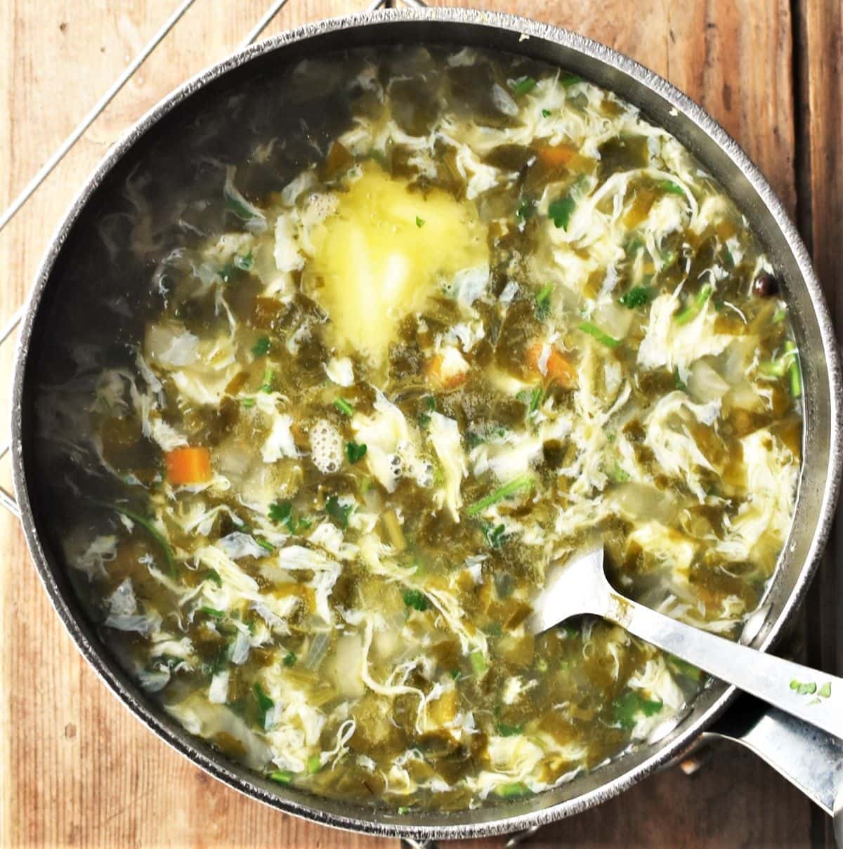Sorrel soup with egg and butter in large pot with spoon.