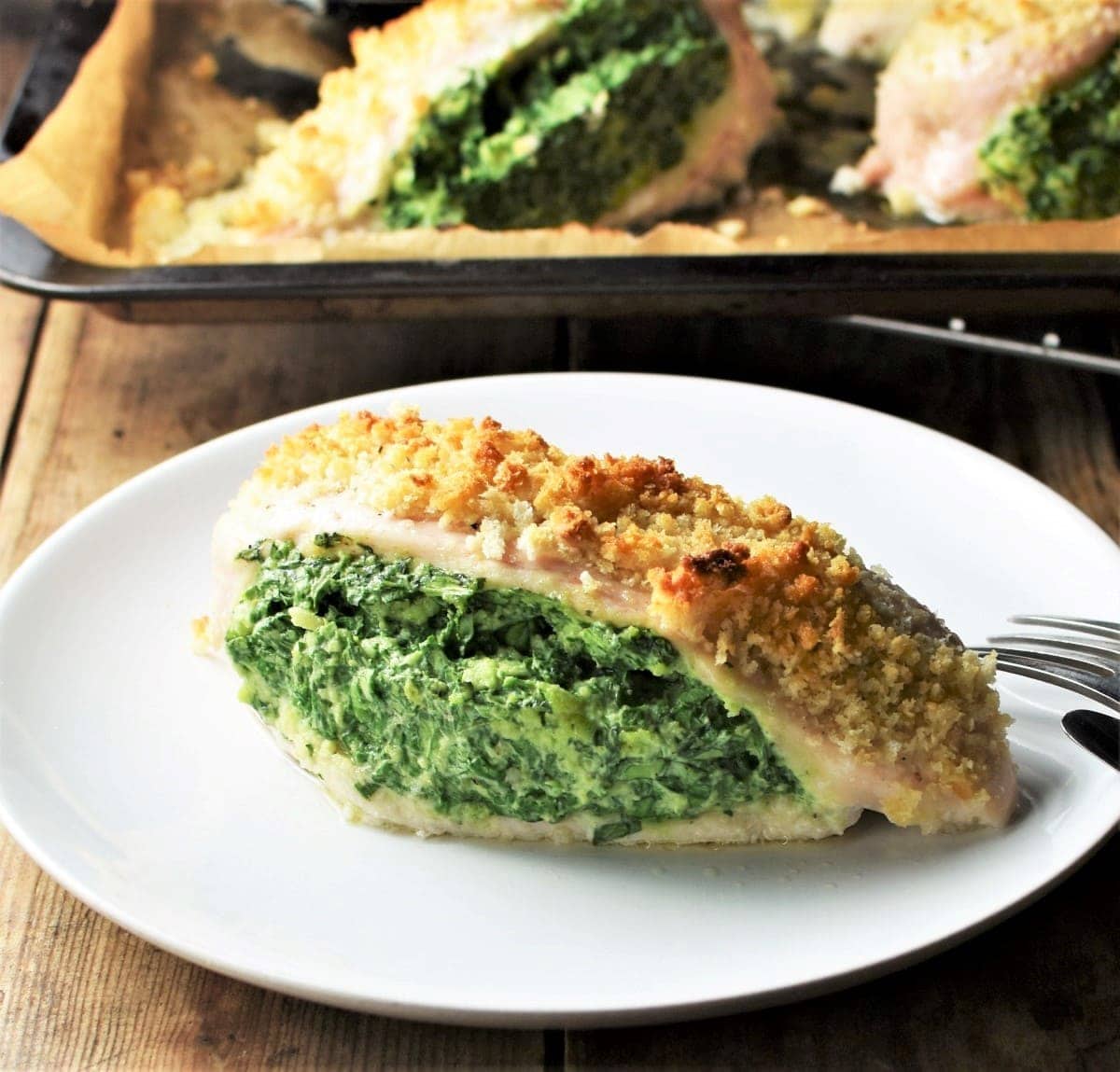 Side view of spinach and cheese stuffed chicken breast on top of plate with chicken in background.