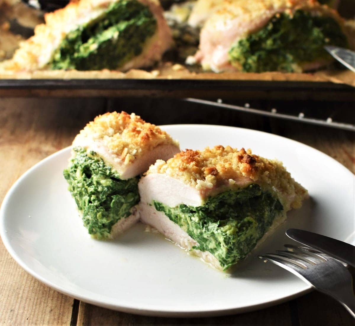 Spinach stuffed chicken breast cut in half on top of plate with chicken in background.