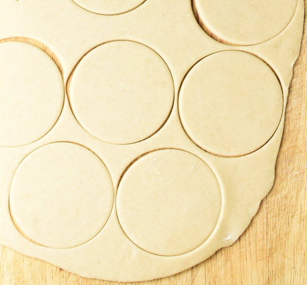 Pierogi dough rounds on top of wooden surface.