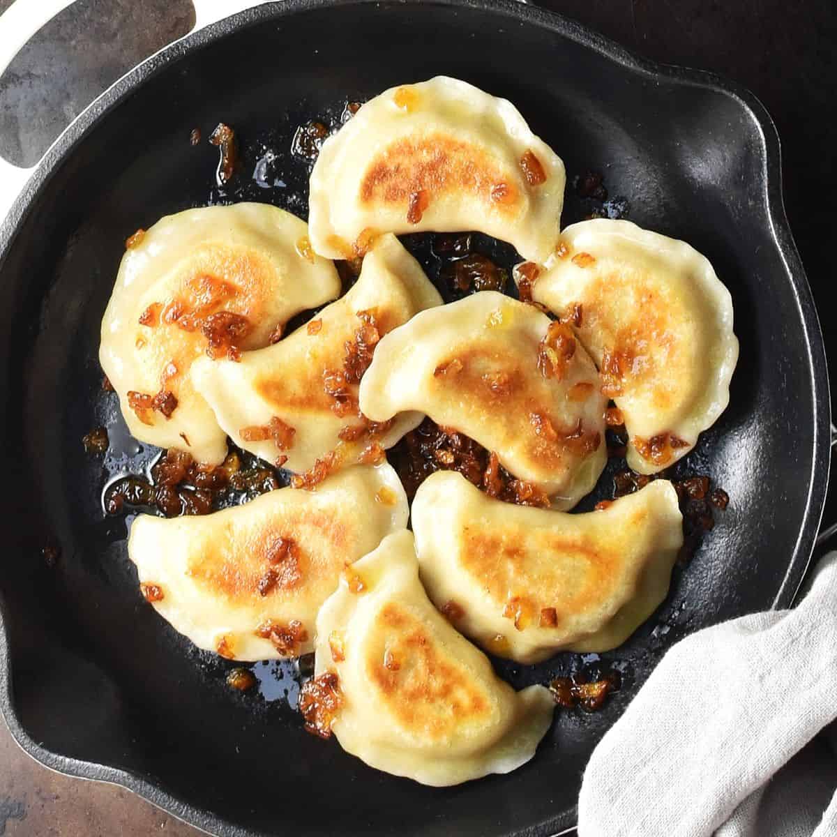 Top down view of browned vegan pierogi with onion incast iron skillet.