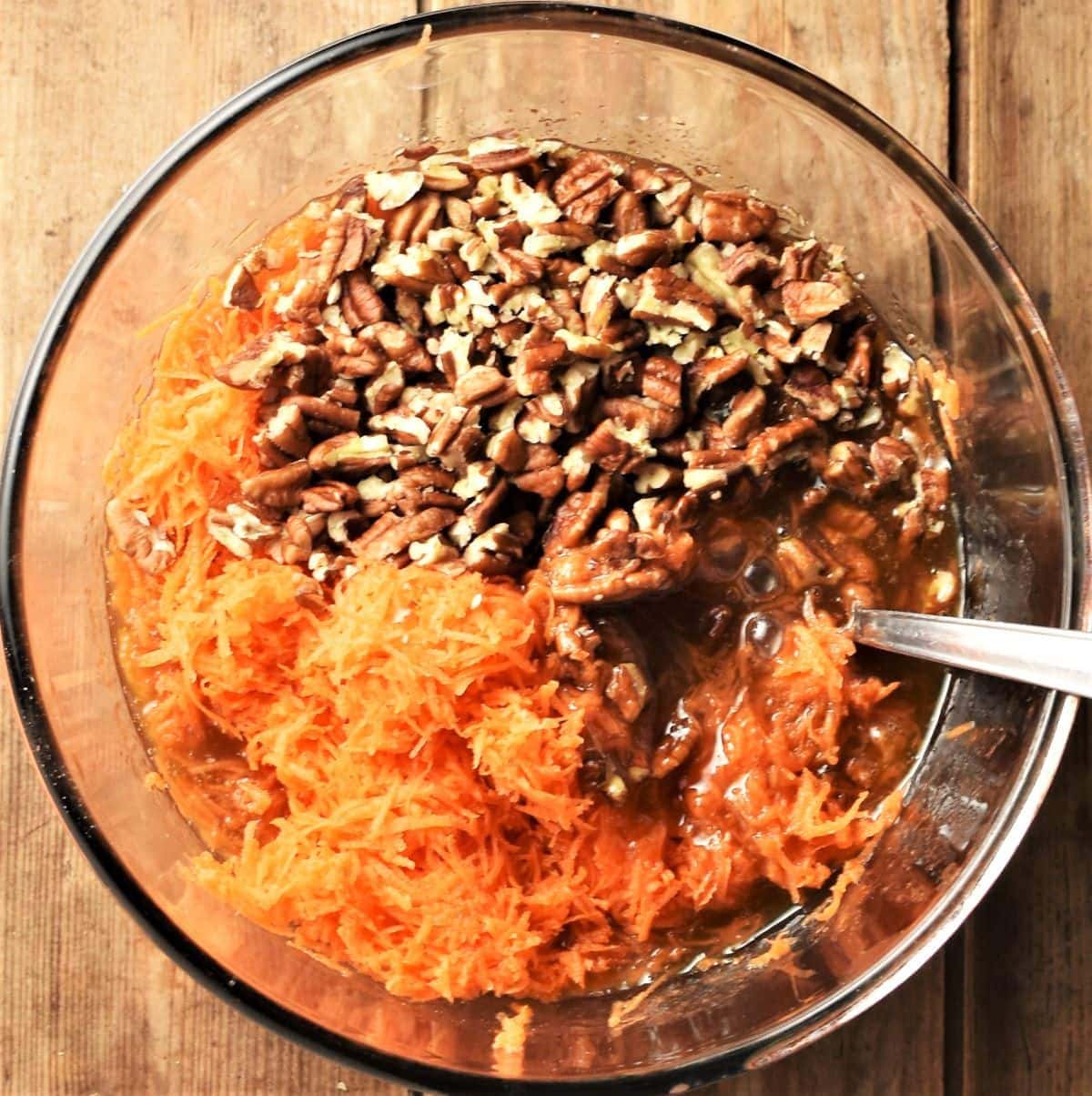 Grated carrot and chopped pecans in mixing bowl with spoon.