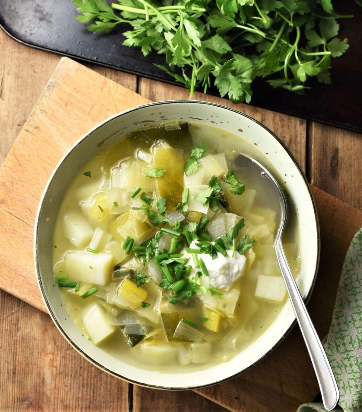 Leek and potato soup in green bowl with spoon and parsley in background.