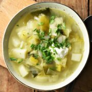 Top down view of chunky leek and potato soup with yogurt and herbs in green bowl.